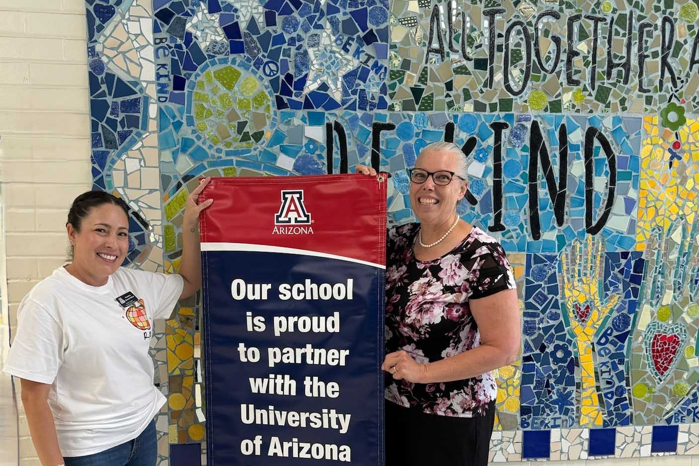 Sewell principal and UA rep with banner reading Our school is proud to partner with the University of Arizona College of Education