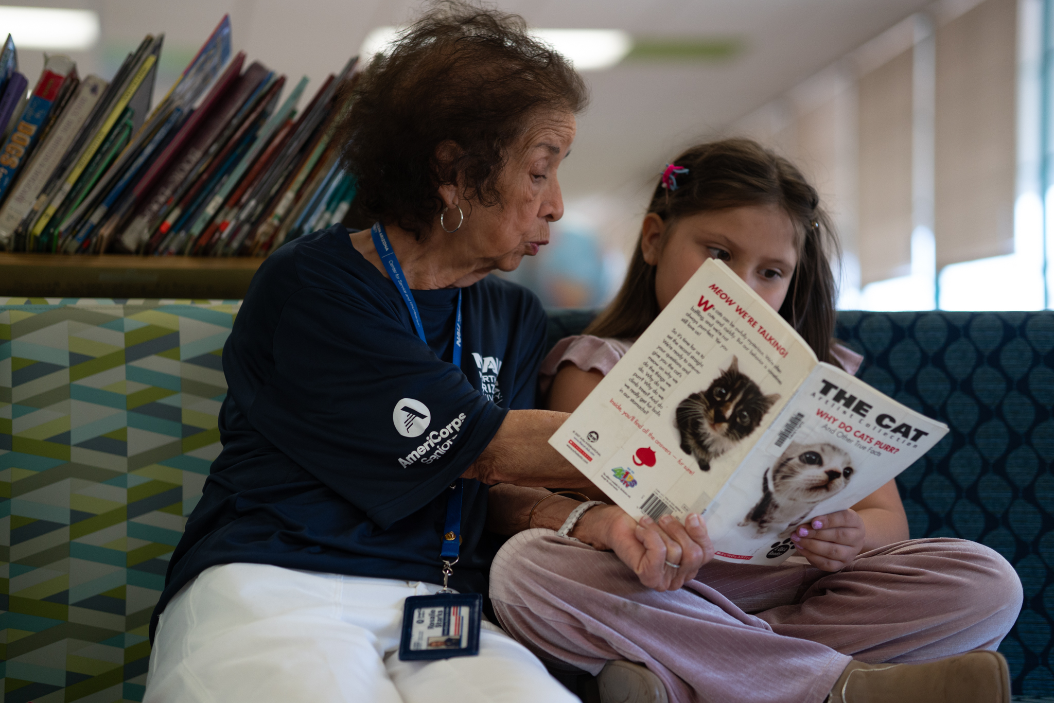 An older woman reads a book about cats with a young girl