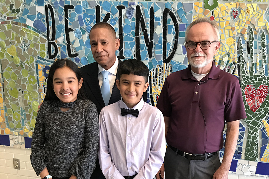 Staff with students in front of a mural that says be kind